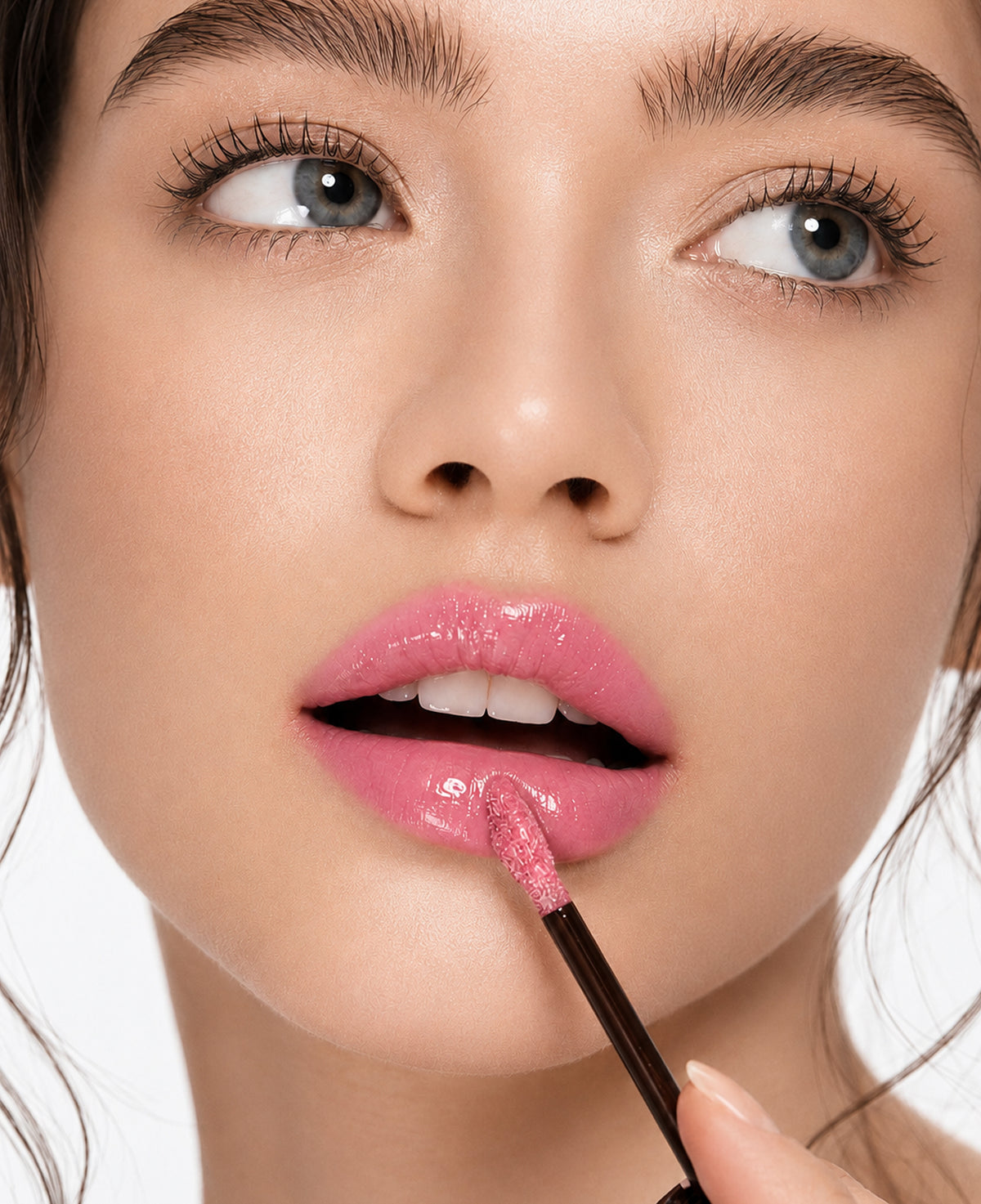 Close-up of a model applying a glossy, sparkly pink lip gloss with a doe-foot applicator to her lips.